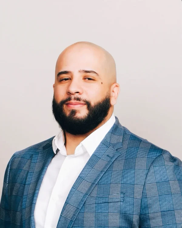 Jason Vargas, Franchise Support Manager at ClawCADE, wearing a blue plaid blazer, smiling confidently against a neutral background.